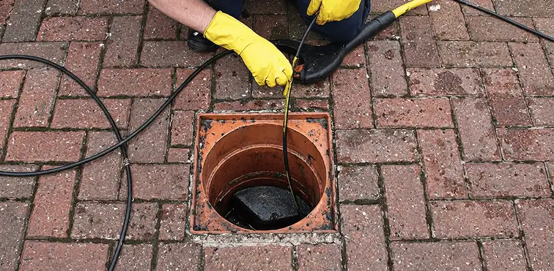 Drain cleaning technician using a drain snake to clear a clogged drain in San Antonio, TX