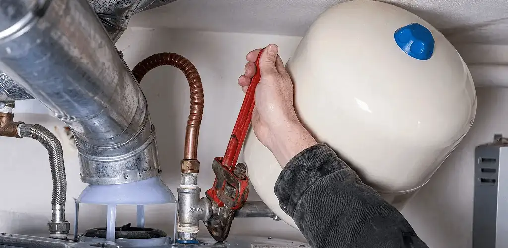 Water heater repair technician tightening plumbing connections near a tank unit in San Antonio, TX